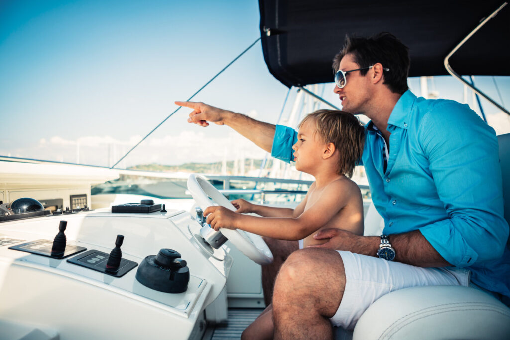 Family Cruisers | Top Yachts & Sailboats for Comfort | YATCO Father teaches his young son how to steer one of the family cruisers.